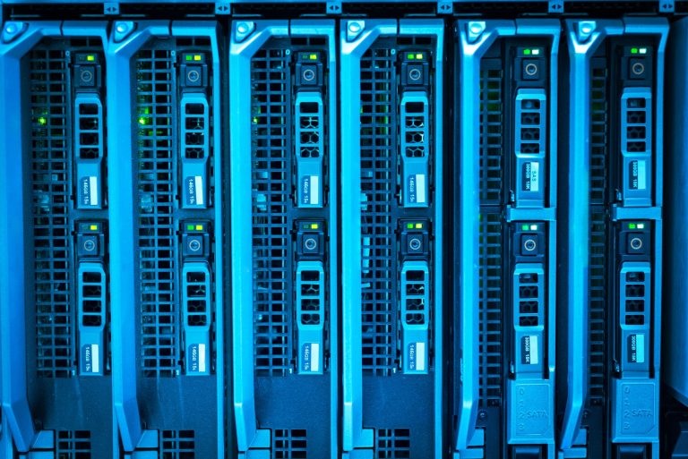 Corredor de datacenter com racks de servidores iluminados em azul e verde.