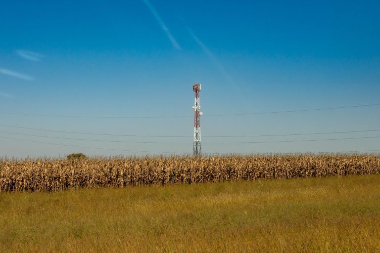 Torre de comunicação em um campo rural sob céu azul.