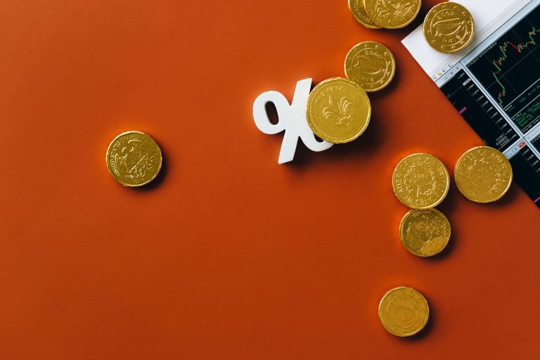 Moedas douradas sobre um gráfico financeiro com símbolo de porcentagem em fundo laranja.
