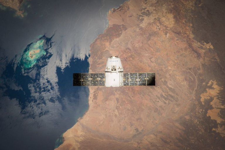 Satélite em órbita sobre a Terra, com oceanos e nuvens visíveis ao fundo.